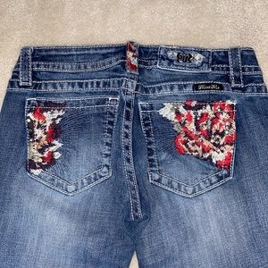 Miss Me signature skinny jeans with multicolored feathered pockets and patches.